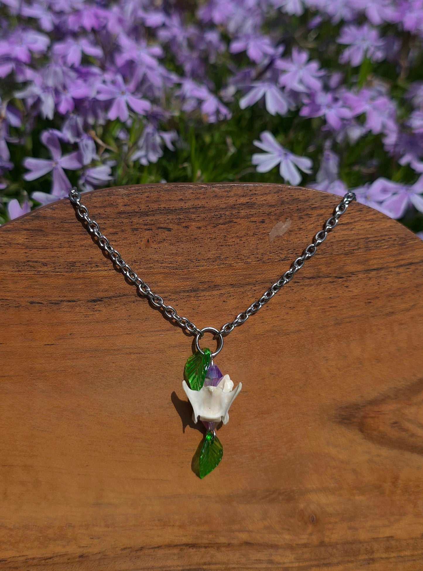 Muskrat vertebrae necklace with two purple beads and leaf charms
 on a wooden surface with purple flowers in the background